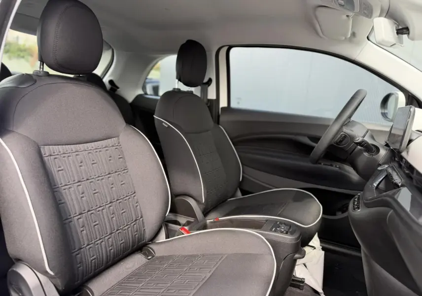Vue intérieure côté droit de la Fiat 500 électrique 2024, sièges tissu noir avec surpiqûres blanches et planche de bord noire.