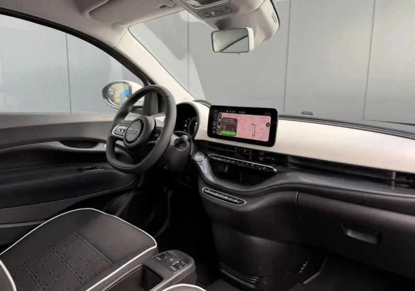Vue intérieure côté conducteur de la Fiat 500 électrique 2024 avec tableau de bord blanc Artic et écran tactile central.
