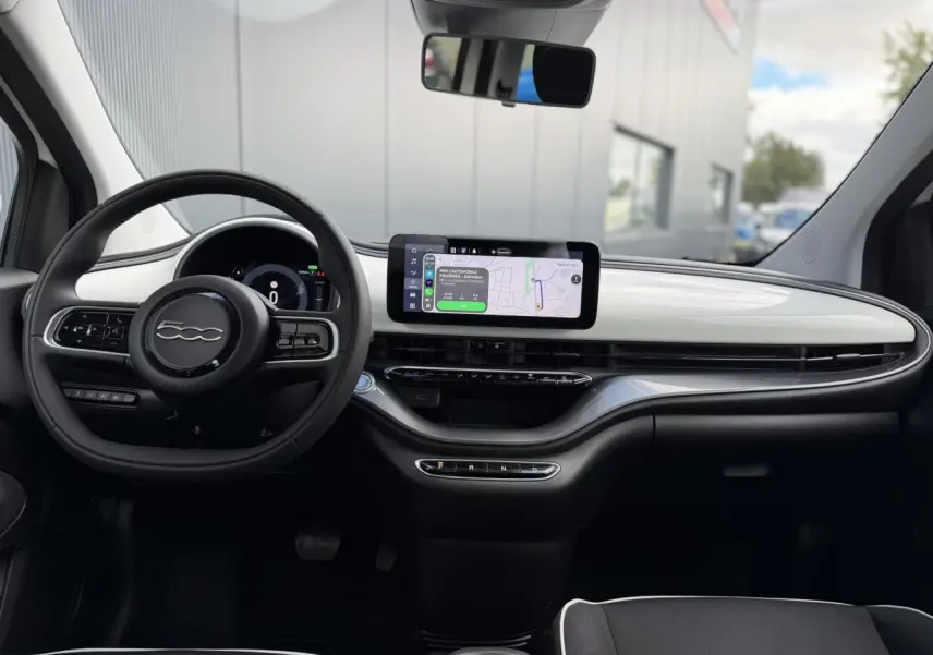 Intérieur du Fiat 500 électrique 2024 vu de face, tableau de bord blanc Artic avec écran tactile central et volant noir Soft-Touch.