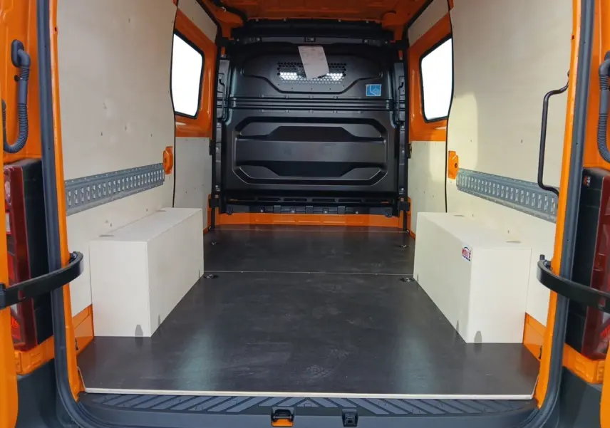 Vue arrière intérieure du Renault Master orange L2H2, montrant l’espace de chargement avec panneaux bois et sol noir.