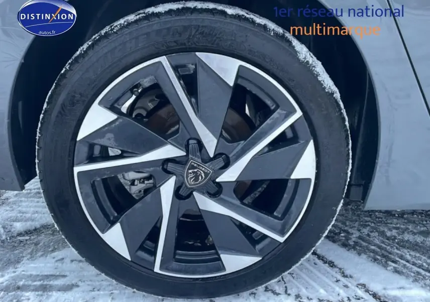 Gros plan sur la jante alu noire et argentée d'une Peugeot 308 gris sélénite, avec logo lion au centre, sur sol enneigé.