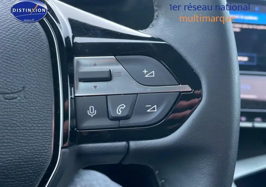 Gros plan sur les commandes au volant à droite d’un Peugeot 308 gris sélénite, avec écran tactile en arrière-plan flou.