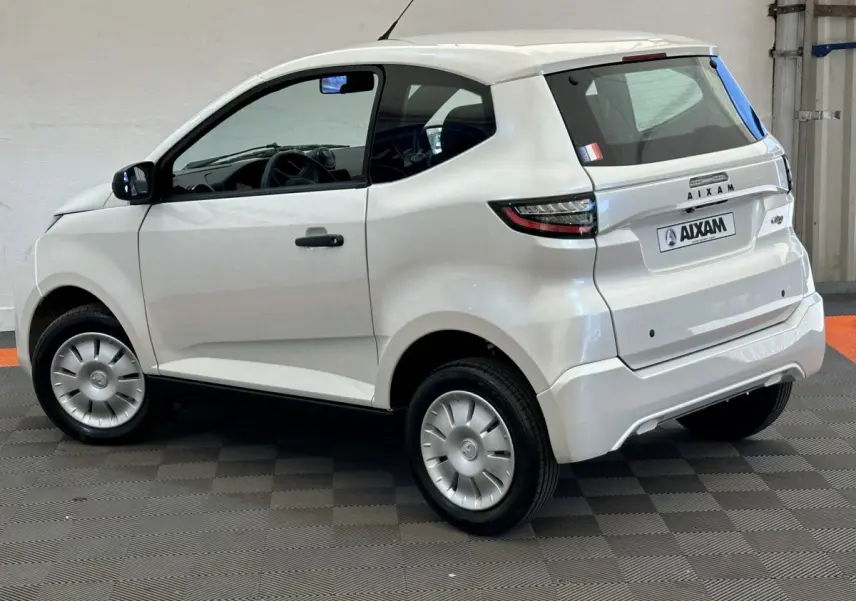 Vue 3/4 arrière côté gauche d'une Aixam Ambition E City Pack blanche 2026 avec rétroviseur caméra côté conducteur.