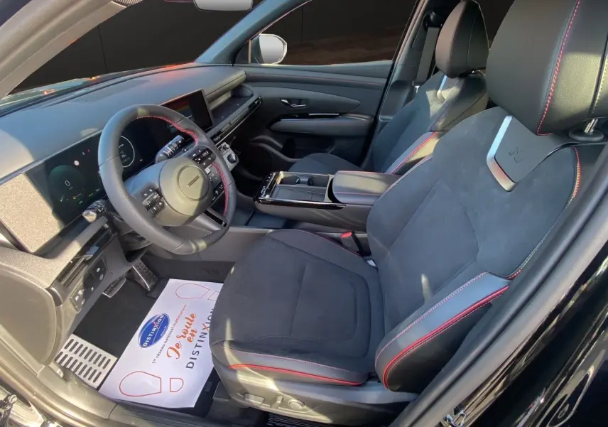 Vue intérieure côté conducteur du Hyundai Tucson 2025 noir abyss, sièges sport noirs avec surpiqûres rouges et tableau de bord moderne.