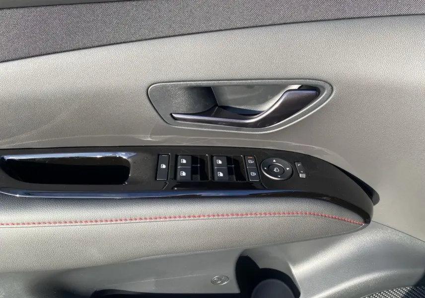 Gros plan sur la porte côté gauche du Hyundai Tucson 2025 noir avec commandes de vitres et poignée intérieure.