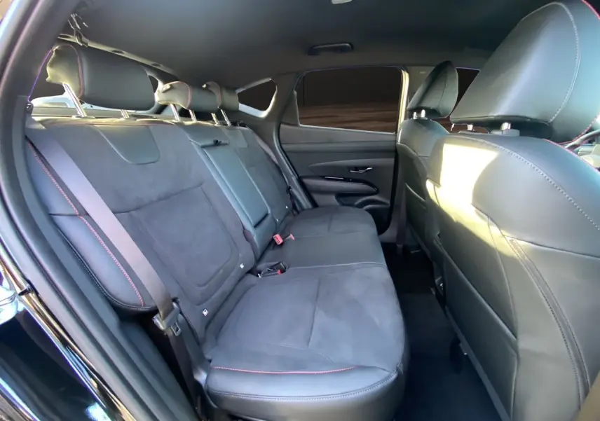 Vue intérieure arrière du Hyundai Tucson 2025 en Abyss Black, sièges noirs en cuir et alcantara avec surpiqûres rouges.