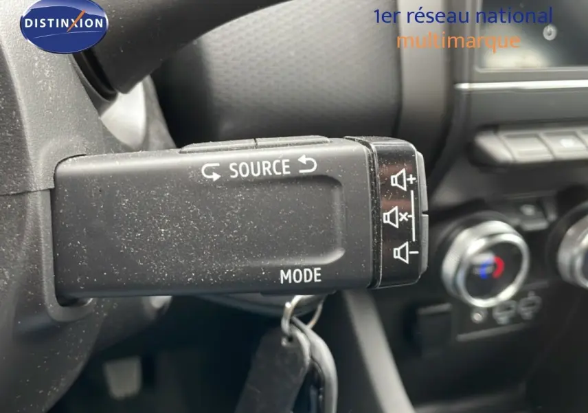 Gros plan sur la commande au volant de la Renault Clio blanche, avec boutons source et mode visibles dans l'habitacle.