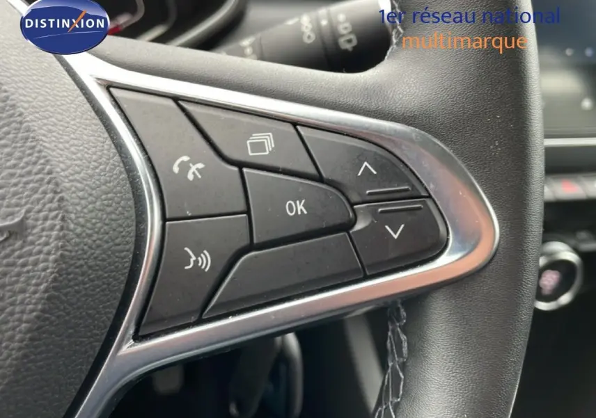 Gros plan sur les commandes multifonctions à gauche du volant cuir noir de la Renault Clio V 1.6 E-TECH blanche.