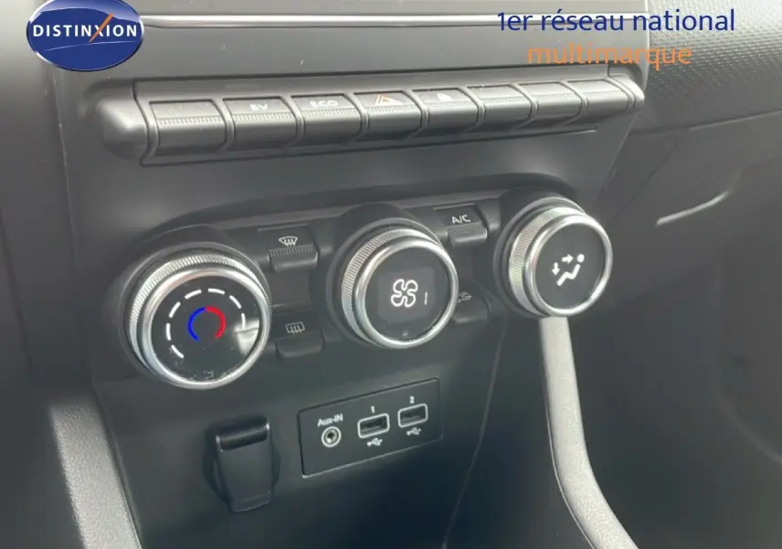 Gros plan sur les commandes de climatisation et les ports USB d’une Renault Clio blanche Glacier, vue intérieure frontale.