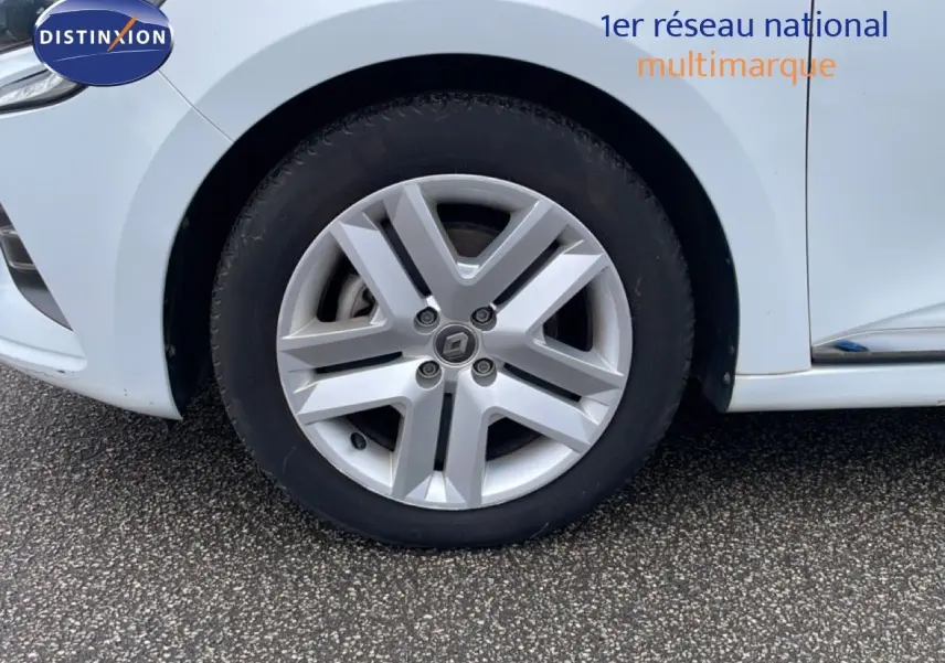 Gros plan sur la roue avant gauche d'une Renault Clio blanc glacier, mettant en valeur la jante alliage distinctive.