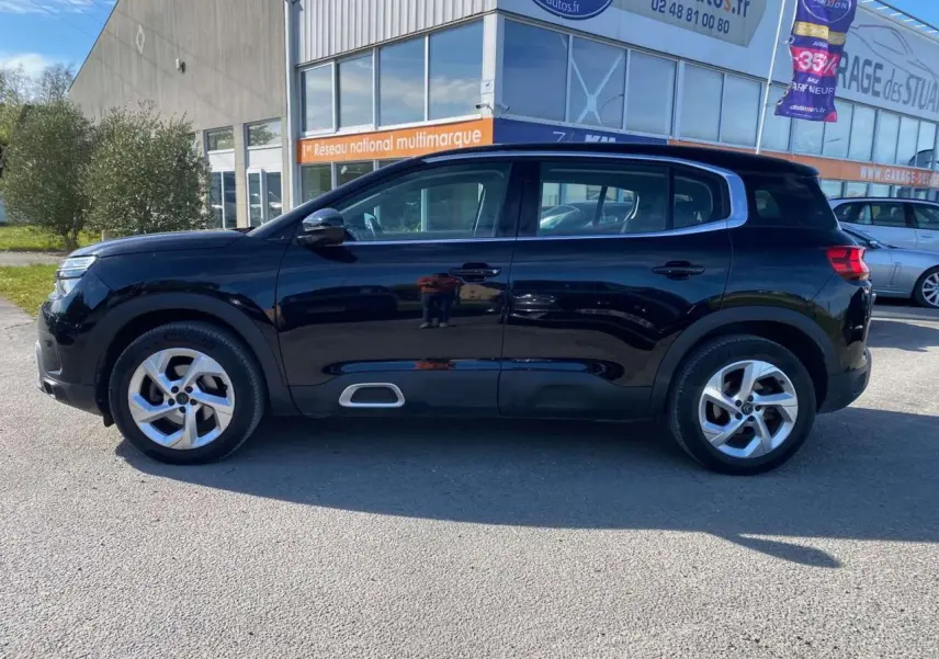 Vue de profil côté gauche d'un Citroën C5 Aircross noir avec jantes alliage 18 pouces, stationné devant un bâtiment.