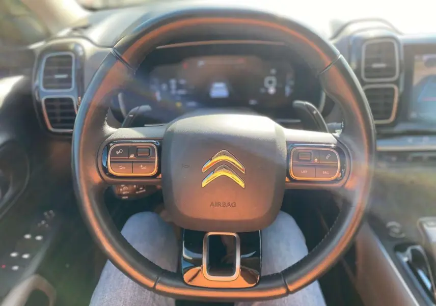Vue rapprochée du volant noir du Citroën C5 Aircross 2021 avec commandes intégrées et tableau de bord numérique flou.