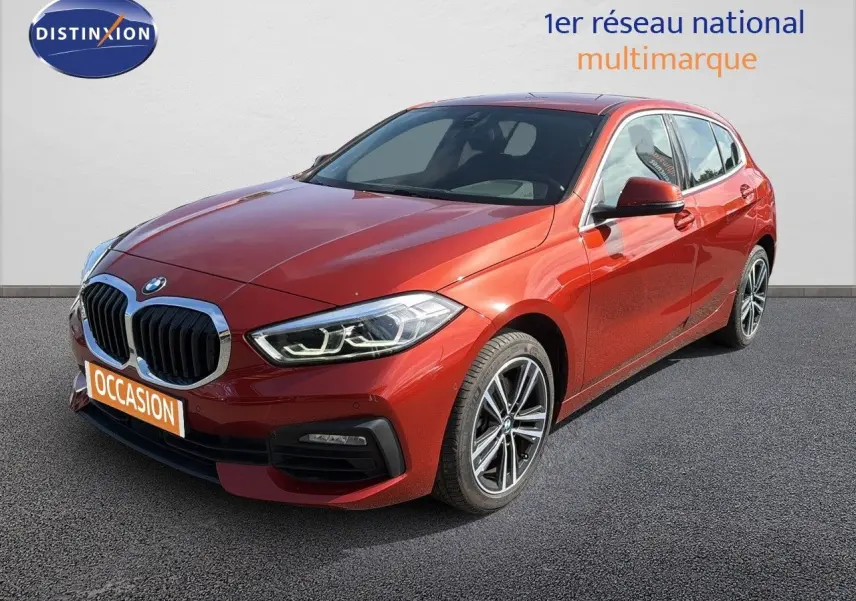 BMW Série 1 116i Business orange Sunset vue 3/4 avant droit, avec calandre imposante et jantes alliage bicolores.