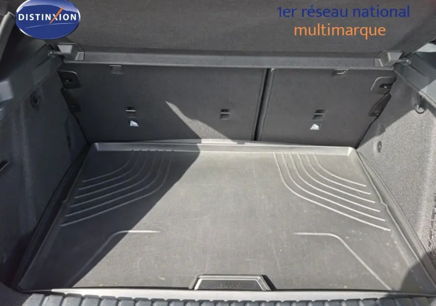 Coffre ouvert vu de face, tapis de sol noir avec logo BMW, intérieur spacieux et revêtement gris foncé.