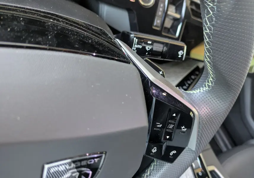 Gros plan sur le volant perforé gris avec surpiqûres vert clair du Peugeot 3008 Hybrid 145 GT, boutons multifonctions visibles.