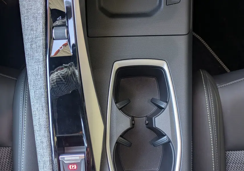 Vue plongeante sur la console centrale du Peugeot 3008 Hybrid 145 GT, avec accoudoir tissu gris et porte-gobelets noirs.