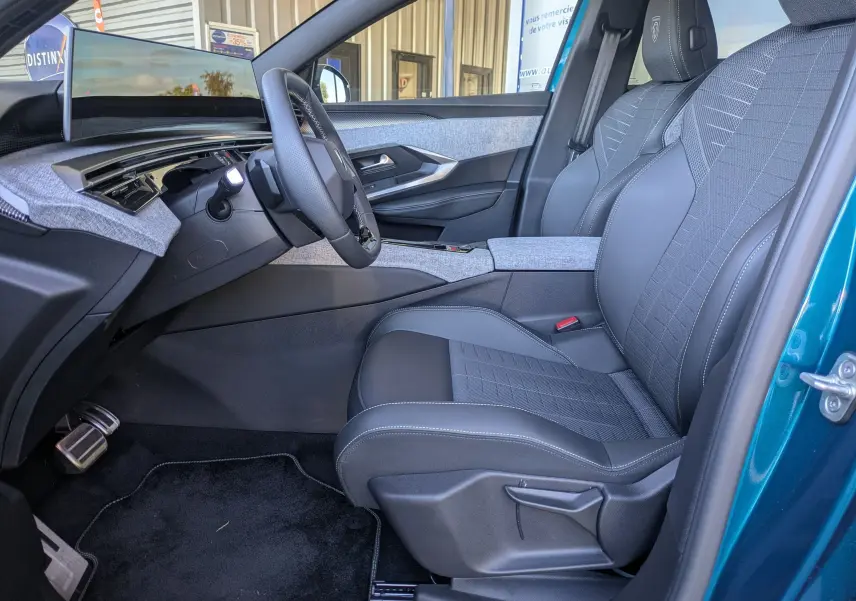 Vue intérieure côté conducteur du Peugeot 3008 Hybrid 145 GT 2025, sièges tissu gris avec surpiqûres et volant multifonction.