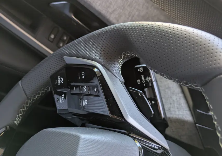 Gros plan sur le volant perforé et les commandes intégrées côté gauche dans l’habitacle du Peugeot 3008 Hybrid 145 GT.