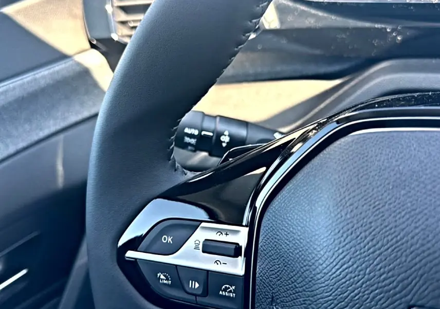 Gros plan sur le volant cuir noir du Peugeot 408 Hybrid 145 allure e-dcs6, avec commandes intégrées côté gauche.