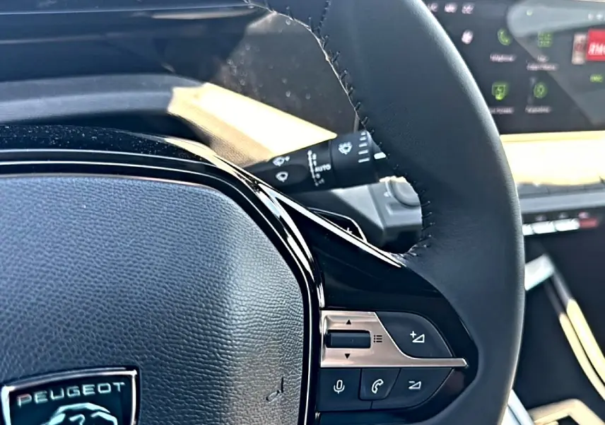 Gros plan sur le volant cuir noir de la Peugeot 408 Hybrid 145 allure, avec commandes audio et téléphone intégrées.