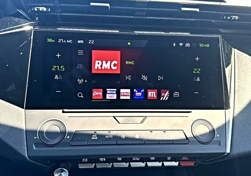 Écran tactile central du tableau de bord du Peugeot 408 noir, affichant la radio RMC et commandes climatisation.