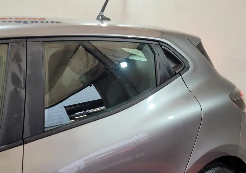 Vue latérale gauche rapprochée d’une Renault Clio gris foncé, mettant en valeur la ligne fluide de la portière arrière.