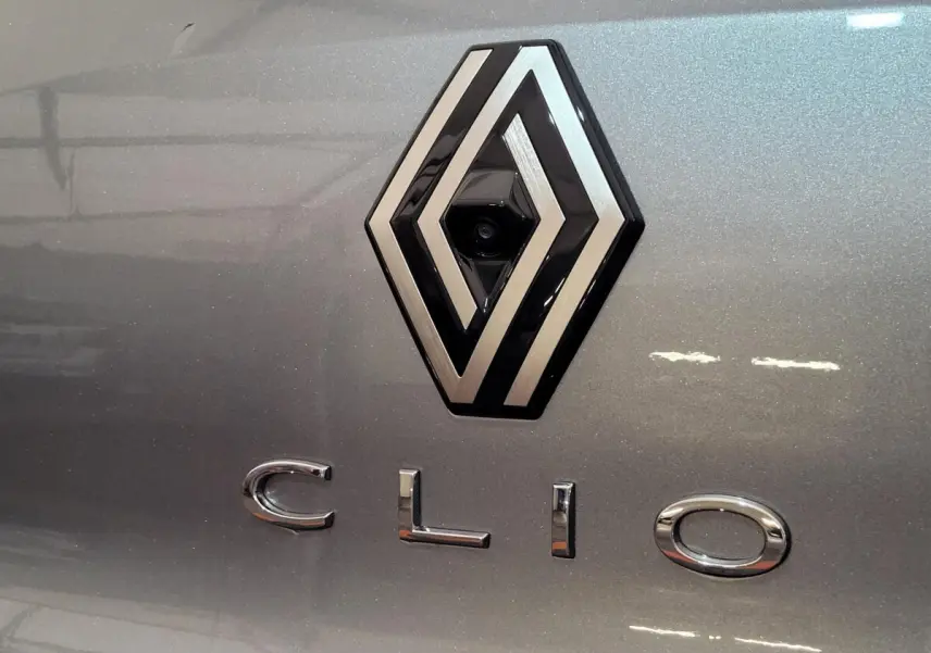 Gros plan sur le logo Renault et l’inscription Clio en chrome sur la carrosserie gris foncé métallisée.