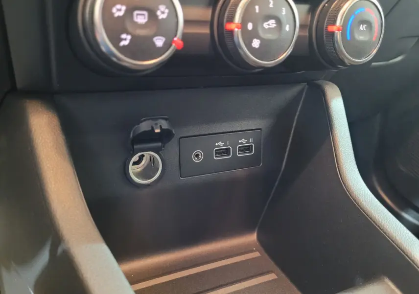 Gros plan sur la console centrale noire de la Renault Clio Evolution Blue dCi 100, montrant les commandes de climatisation et ports USB.