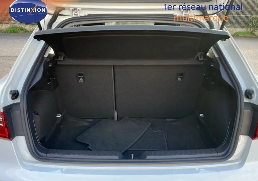 Coffre ouvert d'une Audi A1 Sportback blanc glacier métal, vue arrière montrant l'espace de chargement avec tapis noirs.