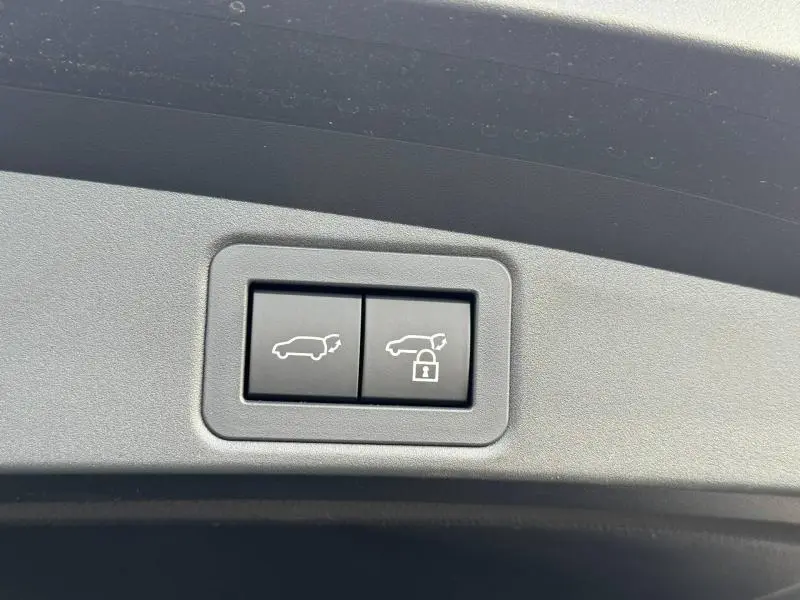 Boutons de commande du hayon avec fonction de verrouillage, sur panneau intérieur gris clair d'une Toyota Corolla noire.