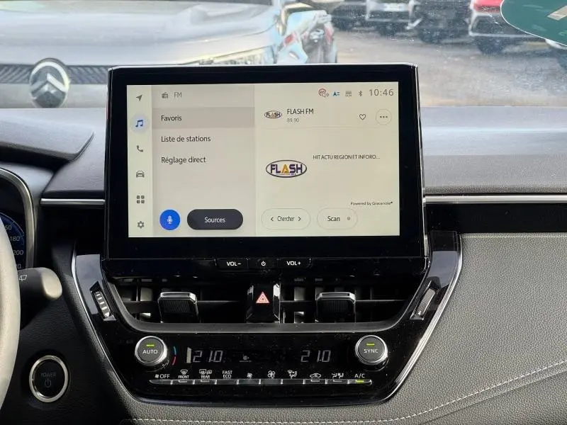 Vue intérieure centrée sur l'écran tactile multimédia de la Toyota Corolla 1.8 HYB Sport PACK TECH noire, avec commandes climatisation visibles.