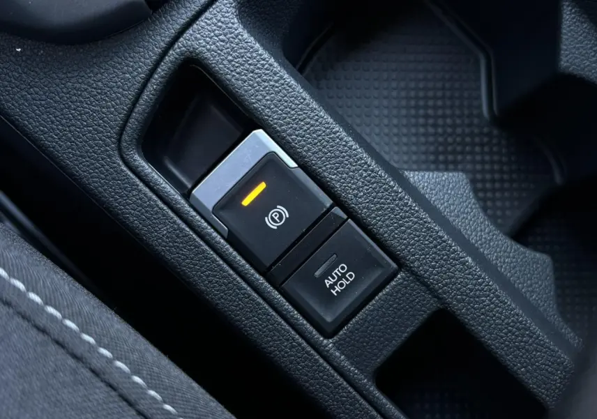 Gros plan sur le bouton de frein de stationnement électromécanique et fonction Auto-Hold dans un Volkswagen T-Roc gris Indium.
