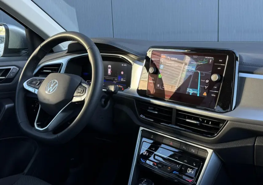 Vue intérieure côté conducteur du Volkswagen T-Roc gris Indium, mettant en valeur le volant multifonction et l'écran tactile central.