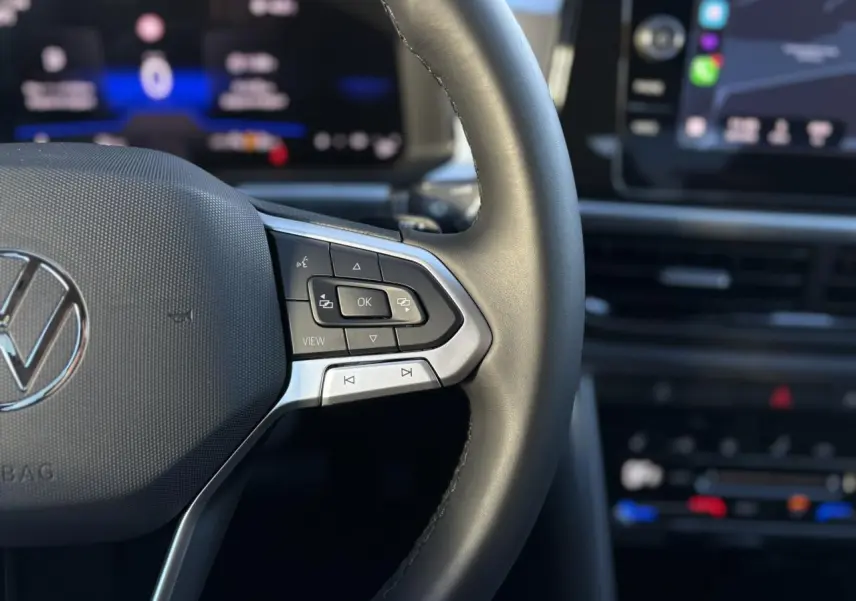 Gros plan sur le volant cuir multifonction du Volkswagen T-Roc 2025 avec commandes intégrées et tableau de bord digital flou.
