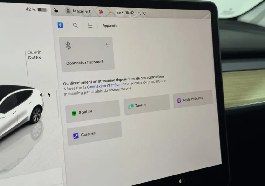 Écran tactile central affichant les options de streaming dans l’habitacle d’un Tesla Model Y blanc, vue intérieure côté passager.