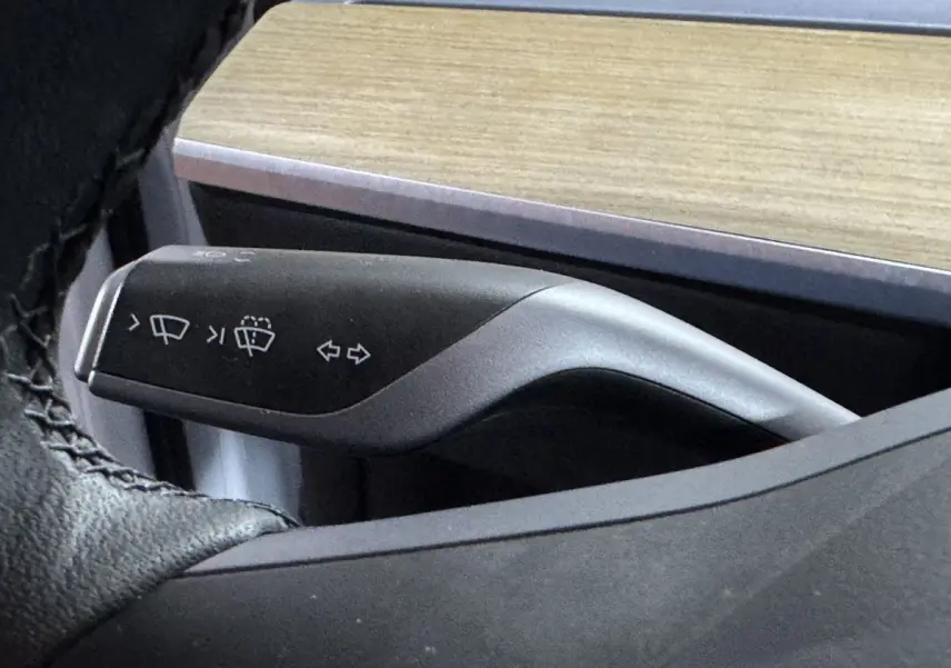 Gros plan sur la commande de clignotants et essuie-glaces noire dans l’habitacle du Tesla Model Y blanc.