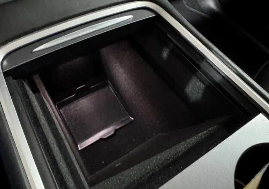 Gros plan sur le rangement central noir avec bordure argentée dans l’habitacle du Tesla Model Y blanc.