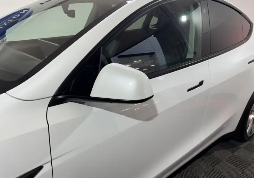 Vue côté gauche rapprochée du Tesla Model Y blanc, mettant en valeur la poignée affleurante et le rétroviseur électrique.
