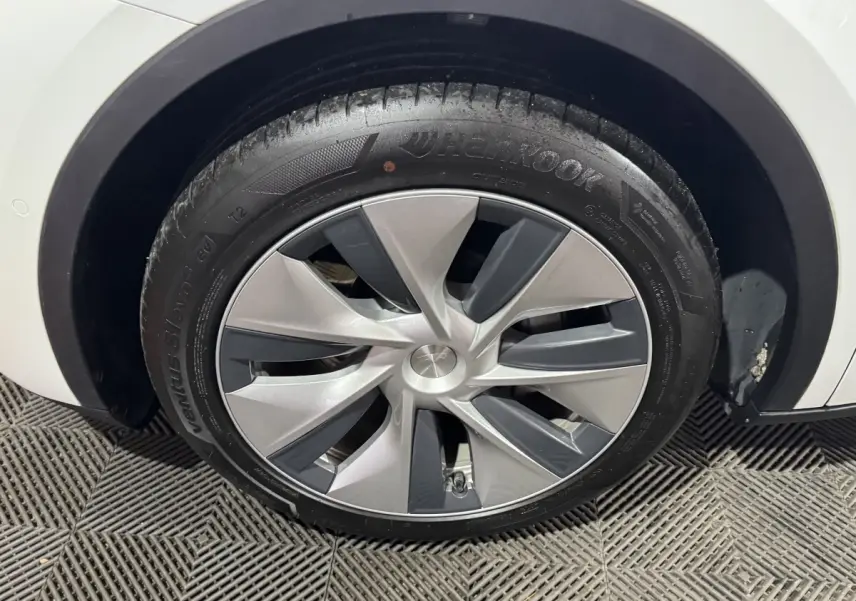 Gros plan sur la roue avant droite d’un Tesla Model Y blanc avec jante aérodynamique grise et noire.