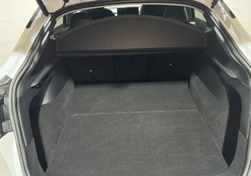 Coffre ouvert vu de l'arrière d'une Tesla Model Y blanc, espace de chargement spacieux et tapis noir.