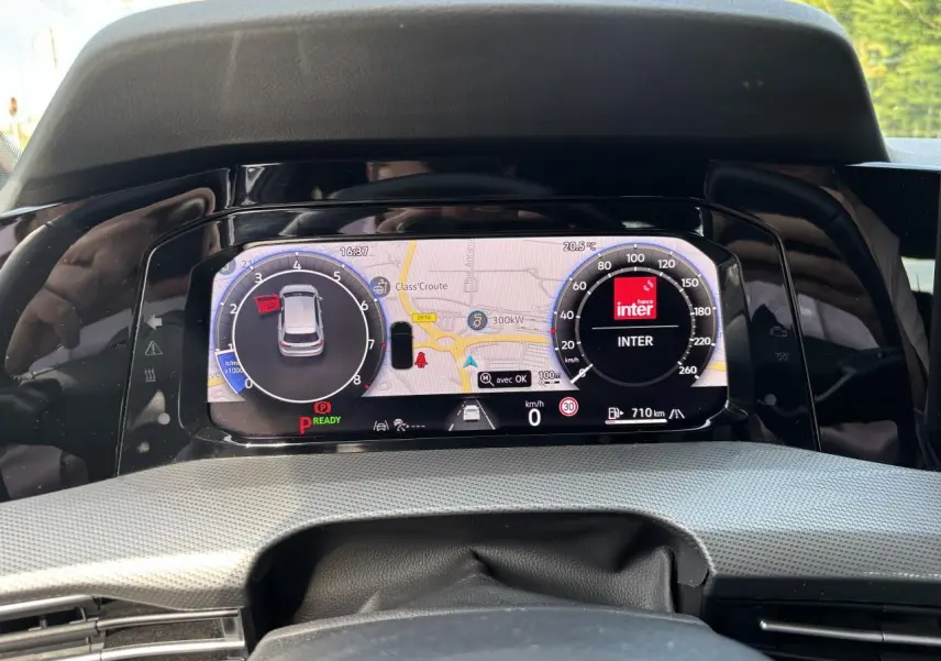 Vue rapprochée du tableau de bord numérique de la Volkswagen Golf blanche 2024, affichant la navigation et la vitesse à 0 km/h.