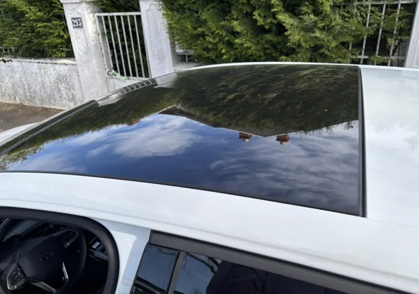 Toit panoramique en verre noir sur une Volkswagen Golf blanche 2024, vue partielle du côté gauche avec volant visible.