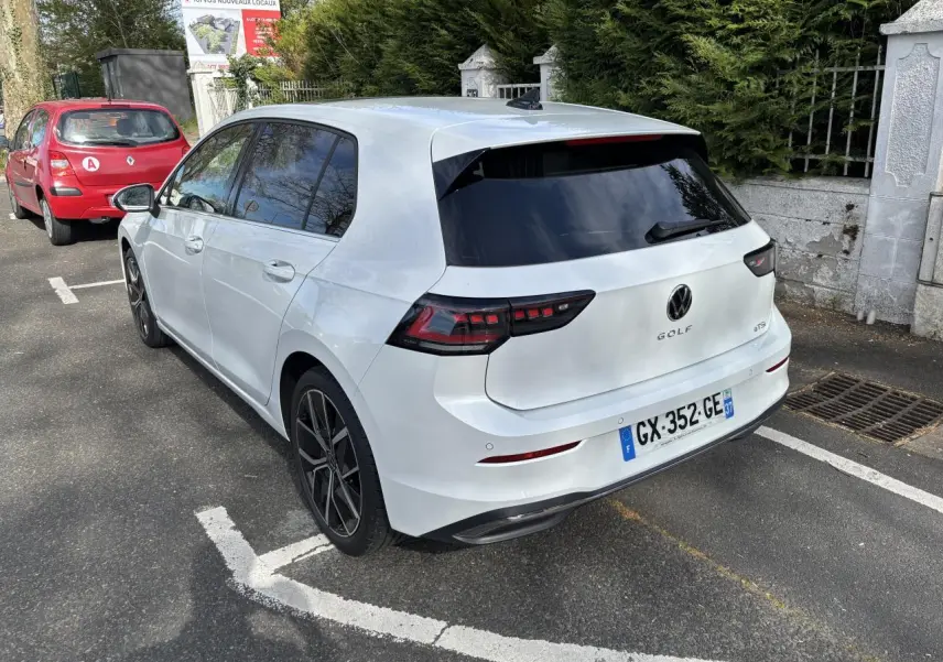 Vue 3/4 arrière droite d'une Volkswagen Golf 1.5 eTSI blanche de 2024, avec vitres teintées et jantes noires distinctives.