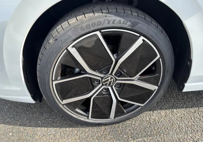 Gros plan sur la roue avant droite d'une Volkswagen Golf blanche 2024 avec jante noire et argentée au design moderne.