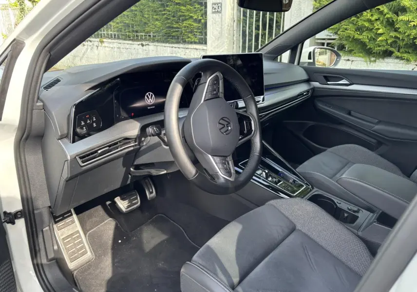 Vue intérieure côté conducteur de la Volkswagen Golf blanche 2024, avec tableau de bord numérique et volant multifonction.