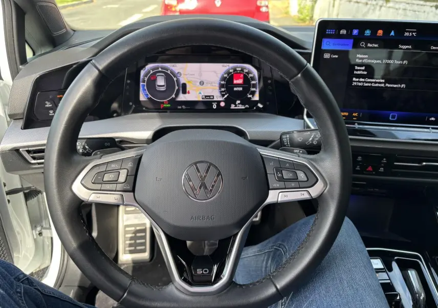 Vue intérieure centrée sur le volant noir de la Volkswagen Golf blanche 2024, avec tableau de bord numérique et logo Edition 50 visible.