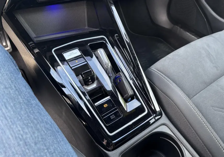 Vue rapprochée de la console centrale noire brillante de la Volkswagen Golf 1.5 eTSI 2024 avec levier de vitesse automatique et bouton start/stop.
