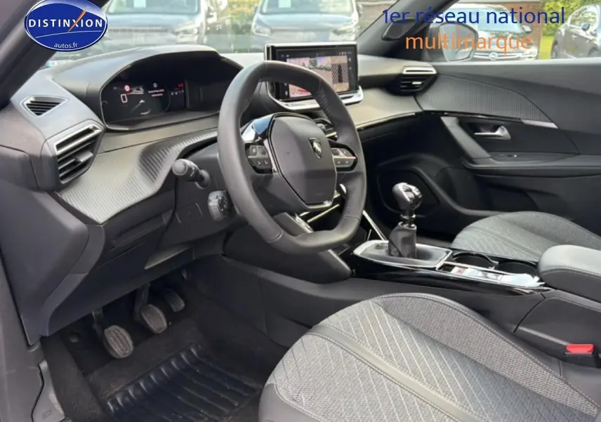 Vue intérieure côté conducteur du Peugeot 2008 1.2 100 allure 2025 avec volant multifonction et sellerie tissu gris.