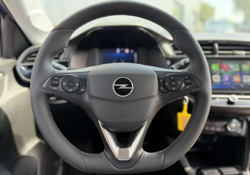 Vue rapprochée du volant en cuir noir de l’Opel Corsa 2025 avec commandes multifonctions et écran tactile en arrière-plan.