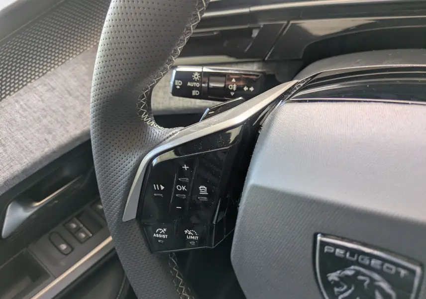 Gros plan sur le volant cuir noir du Peugeot 3008 Hybrid 145 GT, avec commandes multifonctions et logo Peugeot visible.